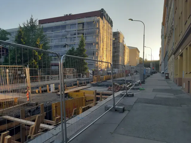 The image shows a city street with a construction site in the middle of it, surrounded by...