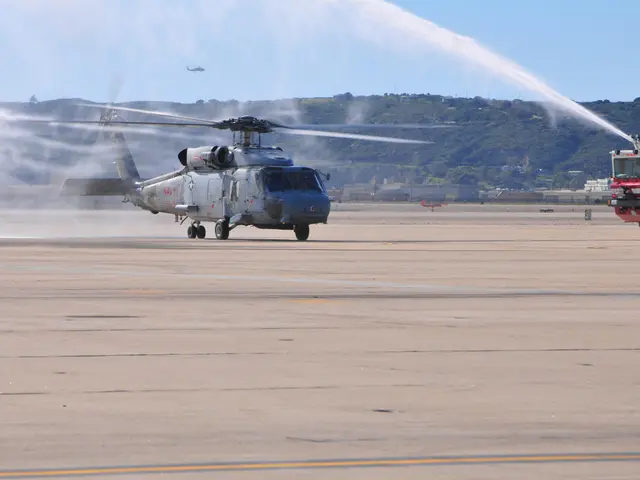 The image shows a helicopter spraying water on an airport tarmac, with a fire truck on the right...