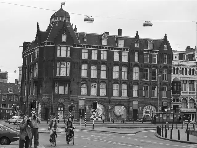 The image shows a black and white photo of people riding bicycles on a city street, surrounded by...