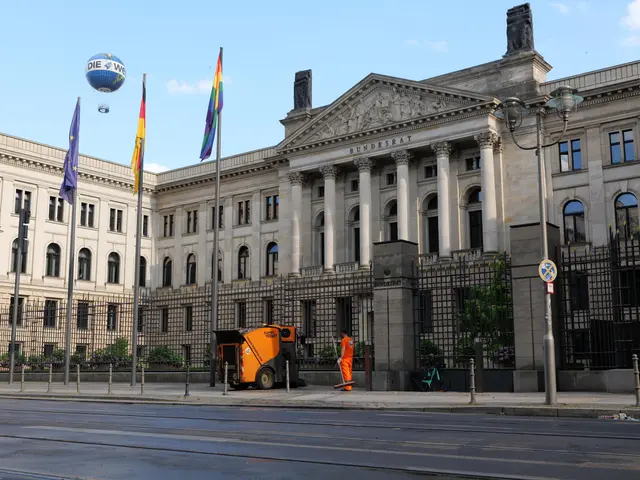 The image shows a large building with a lot of windows on the side of it, surrounded by street...