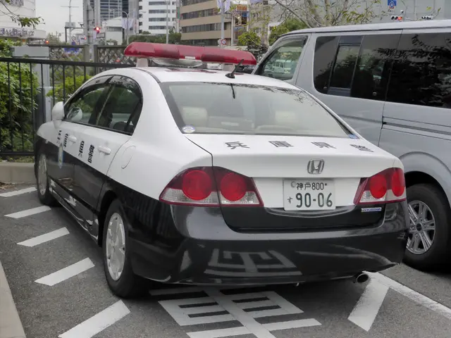 The image shows a police car parked in a parking lot next to a white van. The parking lot is...