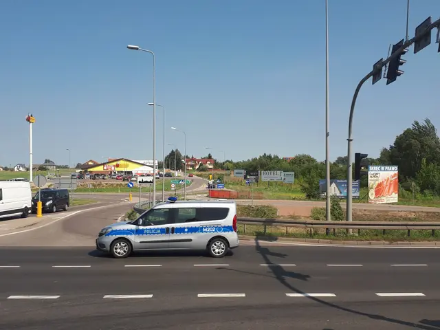The image shows a police car driving down a street next to a traffic light, surrounded by street...