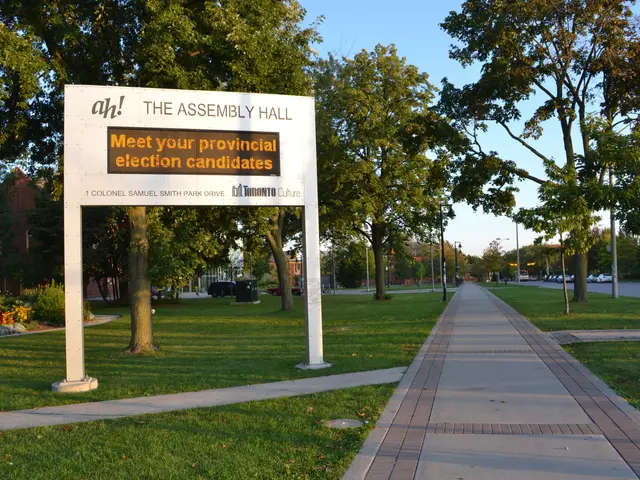 The image shows a board with text on it placed on the ground surrounded by grass, a pathway, a...