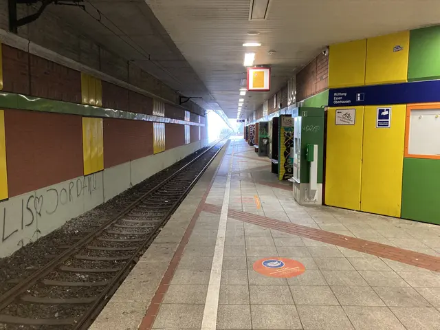The image shows a train station with a train on the tracks, illuminated by lights attached to the...