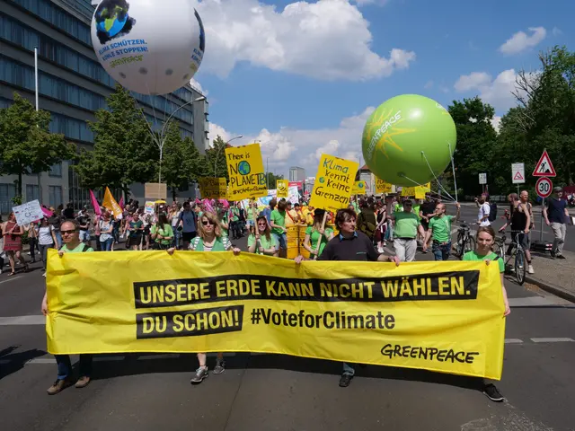 The image shows a group of people walking down a street, holding a yellow banner with the words...