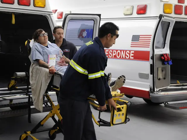 The image shows a woman being loaded into an ambulance by emergency personnel. She is sitting on a...