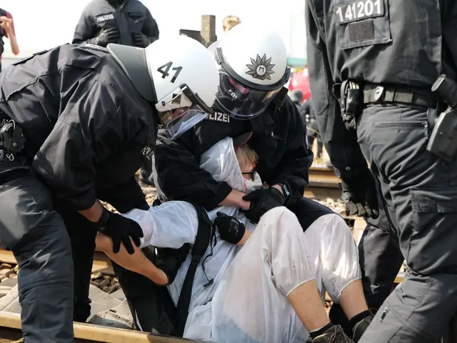 The image shows a group of police officers in riot gear arresting a man on a train track. The man...