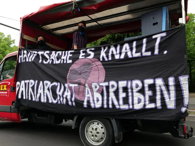 The image shows a red truck with a banner on the back of it driving down a road surrounded by trees...
