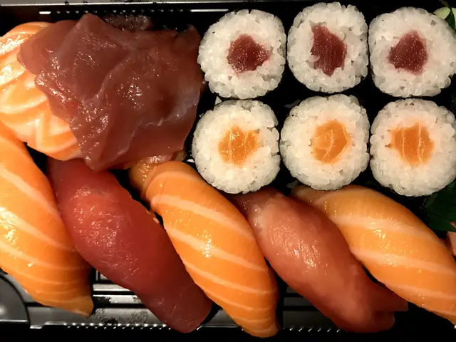 The image shows a black box filled with a variety of sushi, including salmon, tuna, and other types...