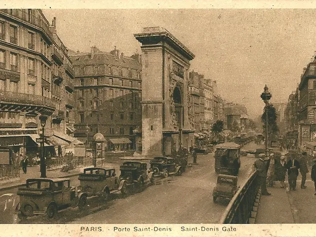 The image shows an old photo of a city street with cars and people. There are buildings with...