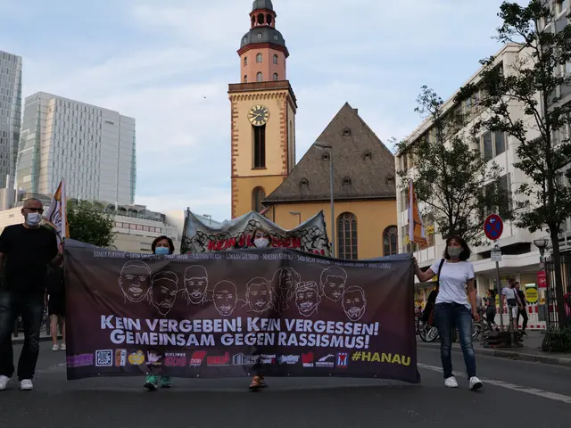 The image shows a group of people walking down a street, holding a banner with text and images on...