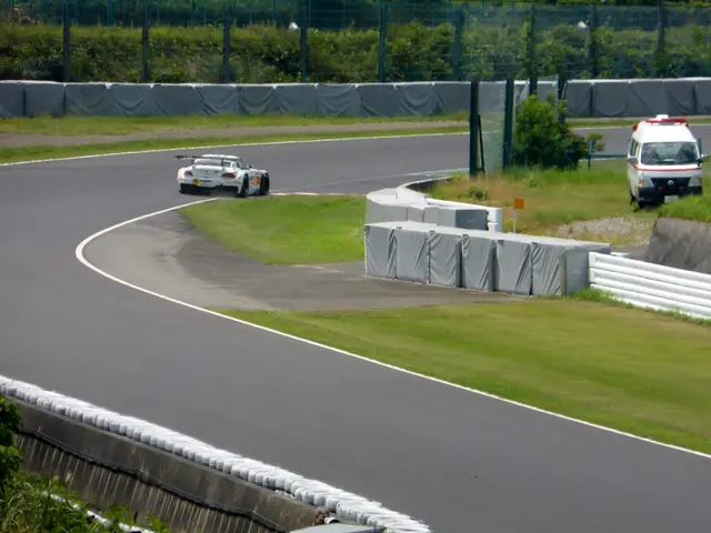 The image shows a race car driving down a race track with a police car in the background. The track...