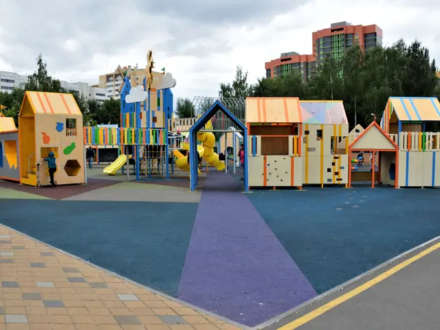 The image shows a children's play area in the middle of a city, surrounded by buildings, trees,...