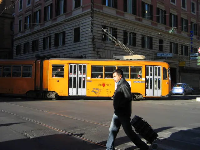 The image shows a man walking down the street with a suitcase in one hand and a trolley in the...