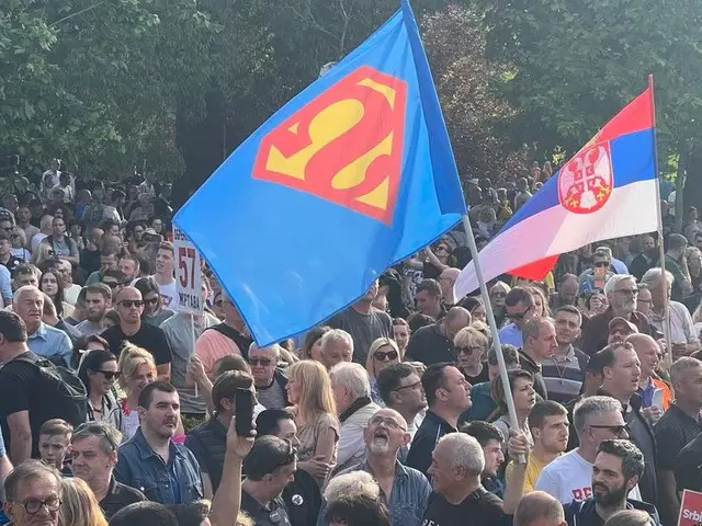 The image shows a large group of people standing in front of a crowd, some of them holding flags...