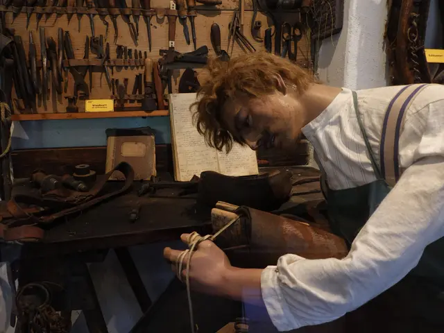 The image shows a man in an apron working on a piece of leather in a workshop. He is holding a tool...