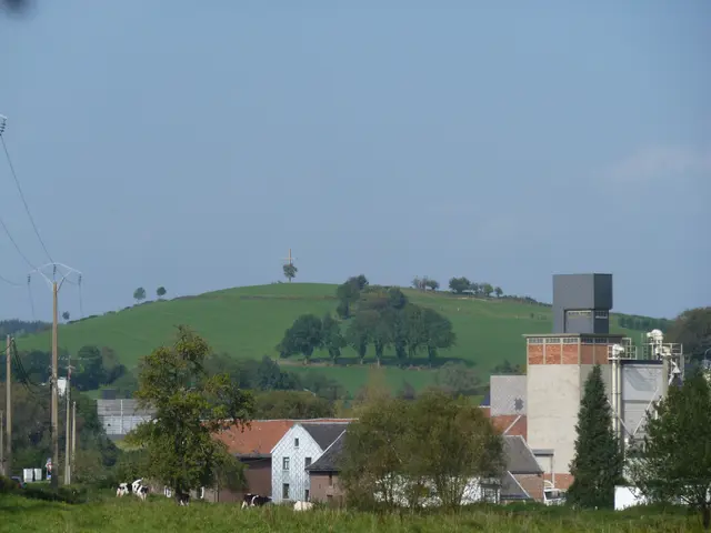 The image shows a farm with cows grazing in a field next to a building, surrounded by trees,...