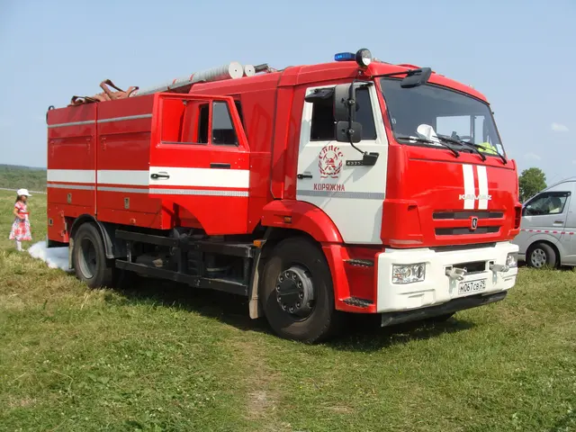 The image shows a red fire truck parked in a grassy field next to a white van. In the background,...