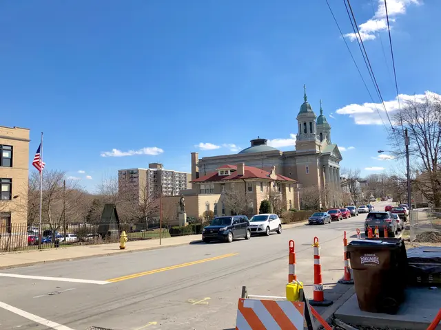 The image shows a city street with cars parked on the side of it, traffic cones, dustbins, a fire...
