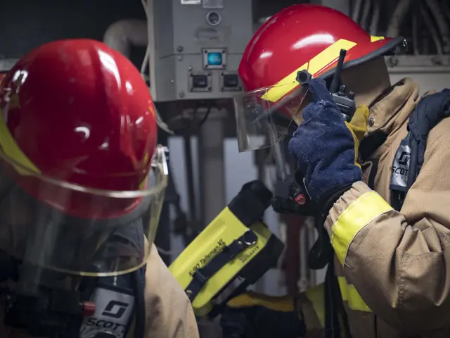The image shows two firefighters wearing protective gear, including helmets and gloves, working on...