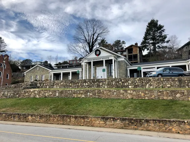 The image shows a stone wall with cars parked in front of it, surrounded by buildings with windows...