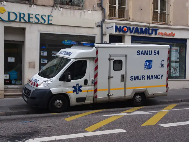 The image shows an ambulance parked on the side of the road in front of a building with windows,...