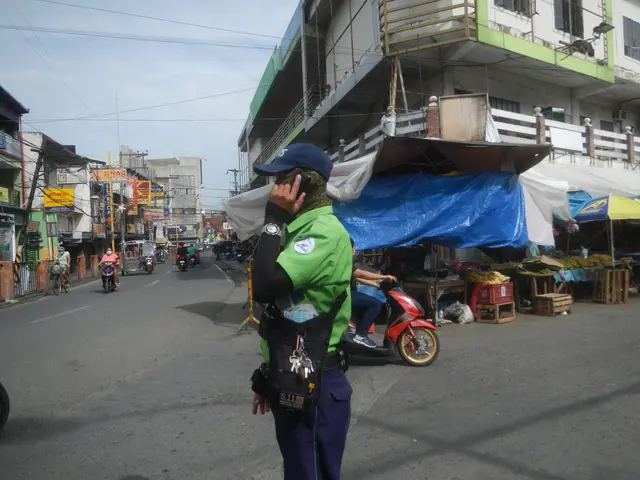 The image shows a police officer standing on the side of a street, talking on a cell phone. He is...