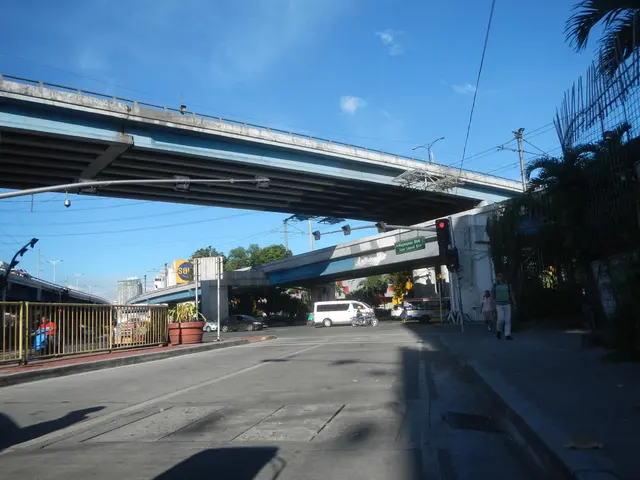The image shows a city street with a pedestrian bridge over it. There are vehicles on the road,...