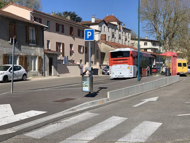 The image shows a bus stopped at a bus stop on the side of a street, surrounded by buildings with...