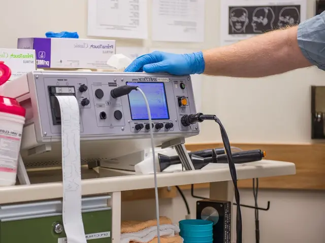 The image shows a person in blue gloves working on a medical device on a table surrounded by boxes,...