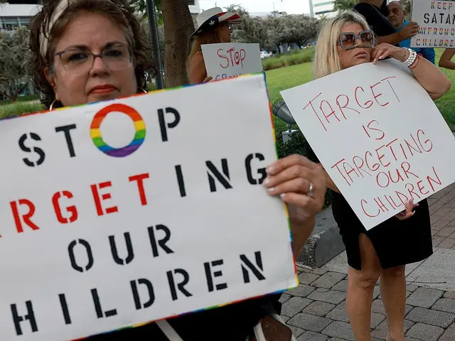 The image shows a group of people standing on the ground, holding signs that read "Stop Targeting...