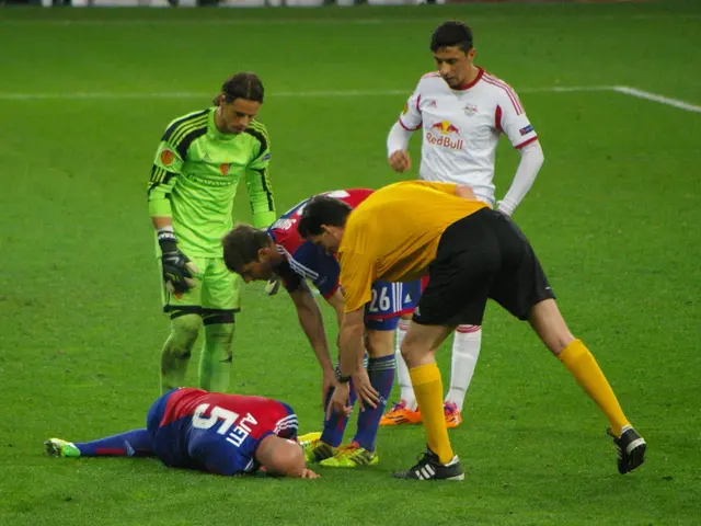The image shows a group of men playing soccer on a field, with one of them lying on the ground. In...