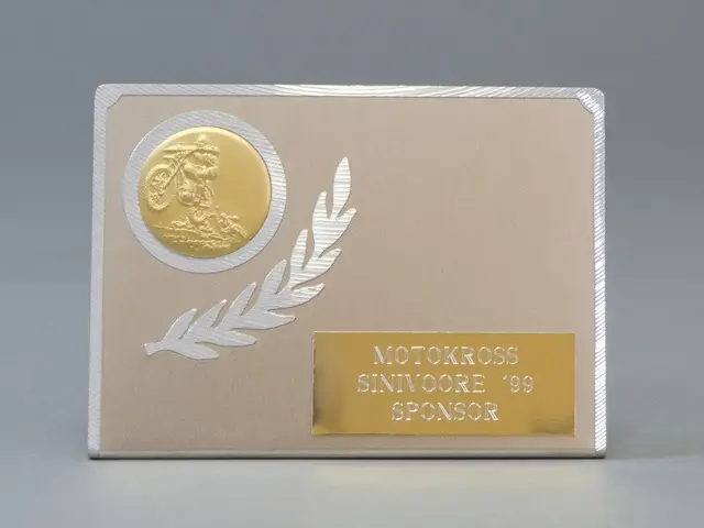 The image shows a gold and silver business card with a laurel wreath on it. The card is in the...