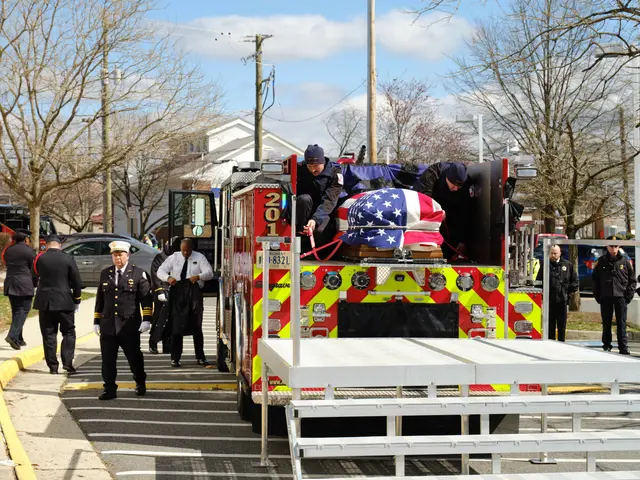 The image shows a fire truck with a casket on the back of it, surrounded by a group of people...