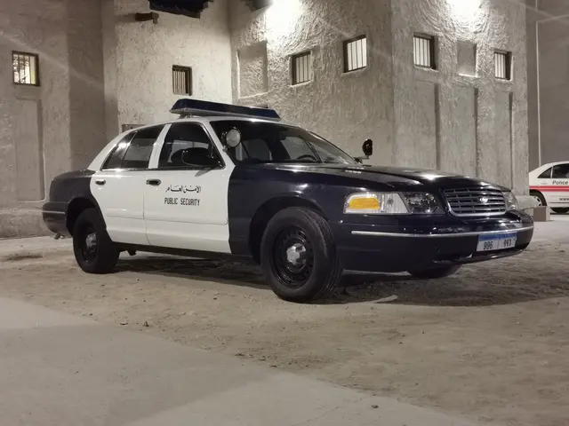 The image shows a police car parked in a parking garage next to a building with windows and lights....