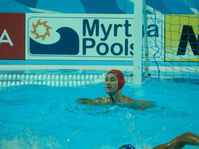 The image shows a water polo player in action in a pool, wearing a cap and swimming in the water....