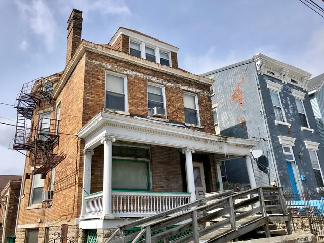 The image shows a row of houses on the corner of a street, with windows, railings, steps, a fence,...