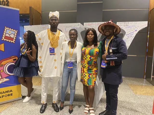 The image shows a group of people standing next to each other in front of a sign, wearing tags and...