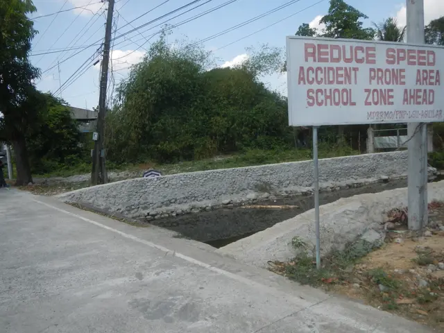 The image shows a road with a sign on the side that reads "Reduce Speed Accident Prone Area School...