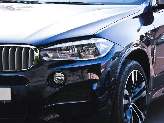 The image shows a black BMW X6 parked in front of a building, with its wheel visible.