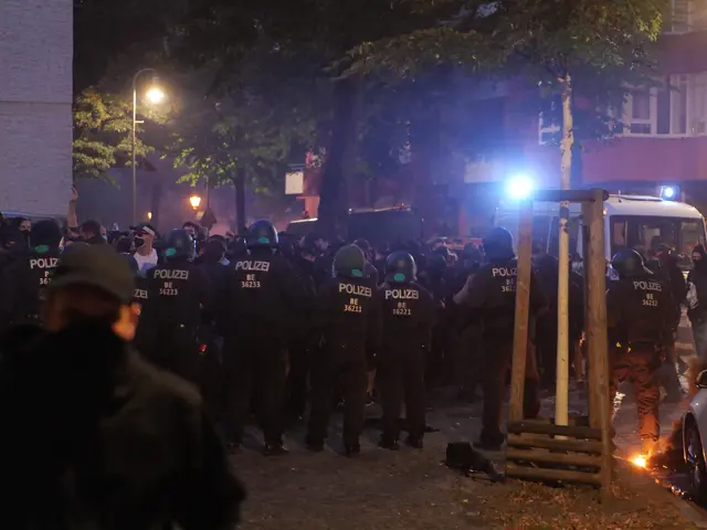 The image shows a group of police officers standing in front of a crowd of people on a road...