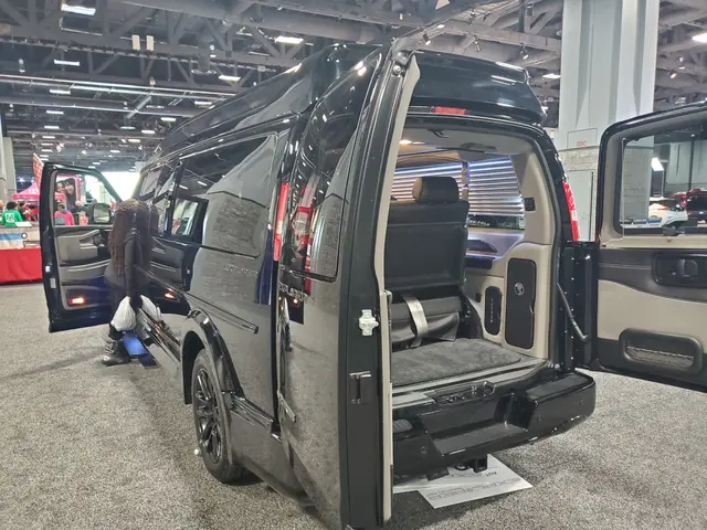 The image shows a black van with its doors open on display at a show, surrounded by a group of...
