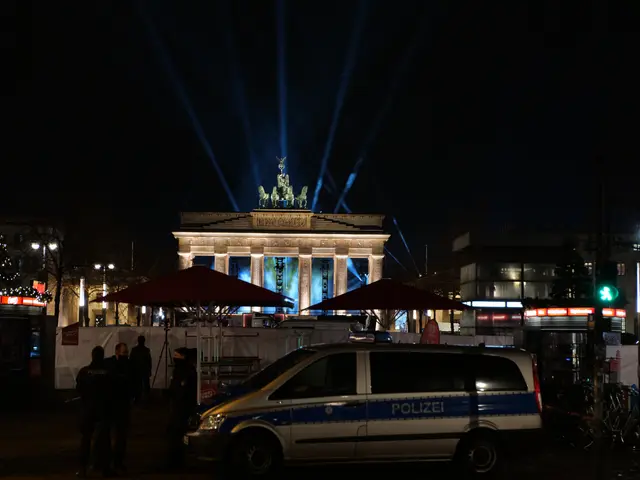 The image shows a police van parked in front of the Brandenburg Gate in Berlin at night. There are...