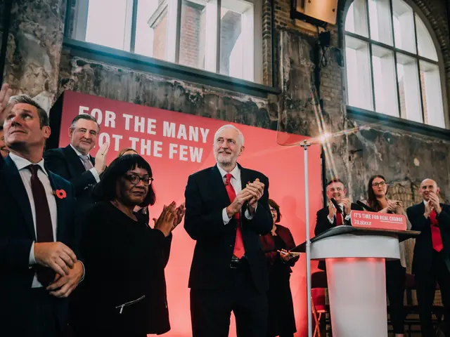 The image shows a group of people standing in front of a podium, clapping their hands in...