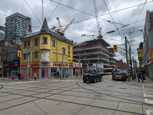 The image shows a city street with cars and people walking on the sidewalk, electric poles with...