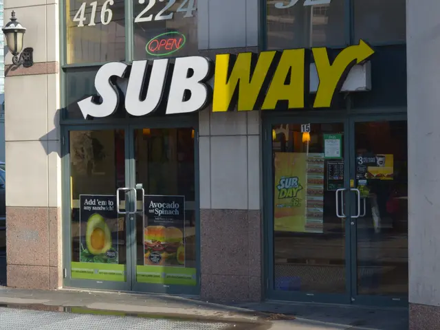 The image shows a subway restaurant on the corner of a street, with glass walls and doors, posters...