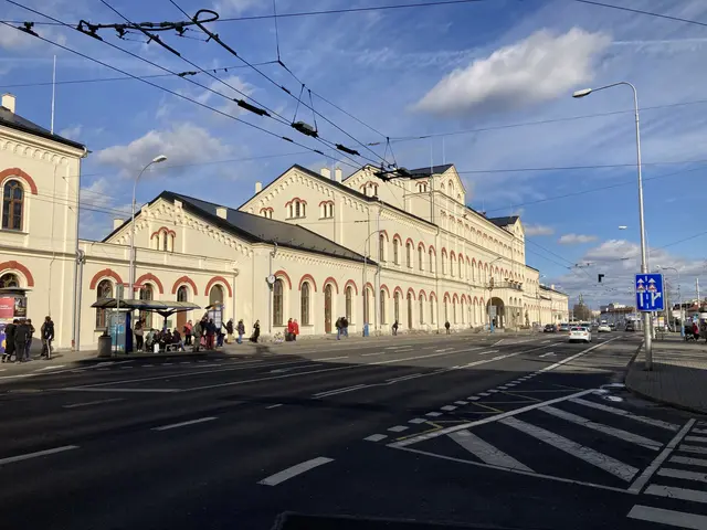 The image shows a city street with a large building on the side of it. There are vehicles on the...