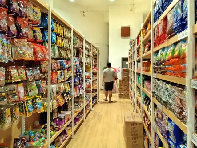 The image shows a man walking down a store aisle filled with lots of different types of food,...