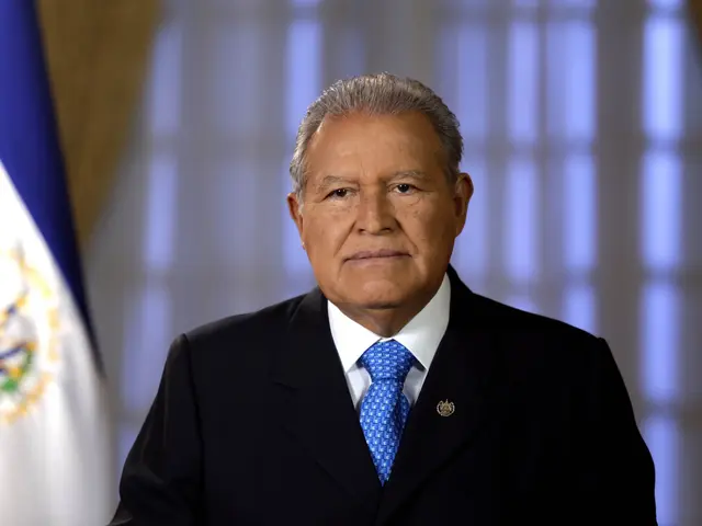 The image shows a man in a suit and tie standing in front of a Mexican flag, with a blurred...