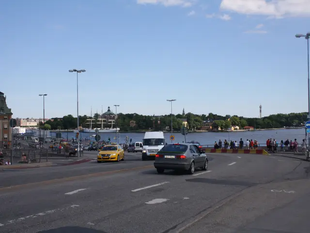 The image shows a city street filled with lots of traffic next to a body of water. There are...